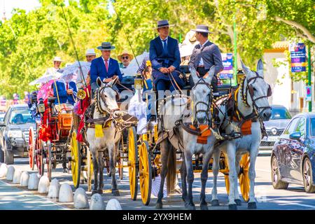 Paesaggio urbano di Siviglia con strade affollate durante la Fiera fiesta di aprile. Auto e carrozze trainate da cavalli si dirigono al festival del patrimonio culturale di Siviglia, in Spagna. Foto Stock