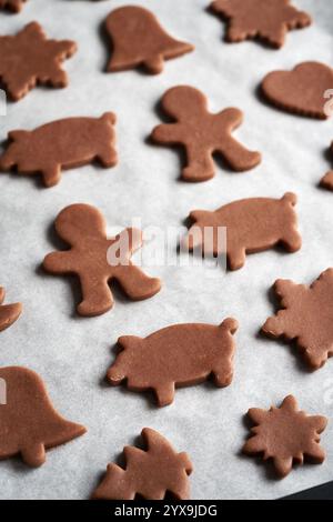 Animali e altre forme tagliate dall'impasto crudo su un foglio di carta da forno - preparazione di biscotti natalizi di pan di zenzero Foto Stock