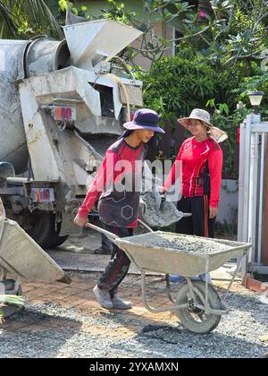Pattaya, Tailandia 29 novembre 2024, individui laboriosi vengono visti trasportare calcestruzzo in carriole, preparandosi per lo stampaggio e la finitura. Foto Stock