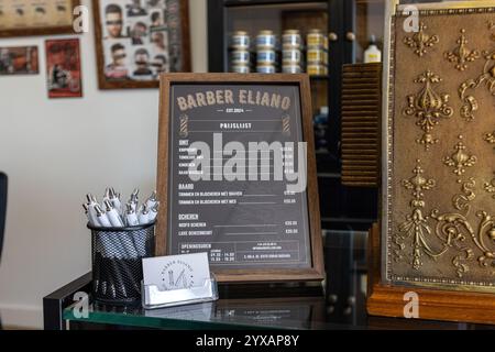 Primo piano del listino prezzi con struttura in legno del Barber Eliano, che presenta tagli di capelli, barba e servizi di rasatura, con penne e biglietti da visita. Foto Stock