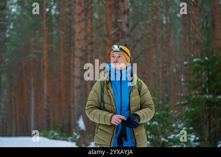 Escursionista maschile, vestito con abiti caldi e un faro, che naviga attraverso una splendida foresta innevata durante l'inverno, abbracciando la bellezza serena e la tranquillità della natura Foto Stock