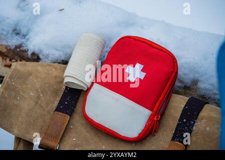 Concetto di preparazione alle emergenze invernali con kit di pronto soccorso e bendaggio posizionati su uno zaino in un ambiente innevato, sottolineando l'importanza della sicurezza durante le avventure invernali all'aperto Foto Stock