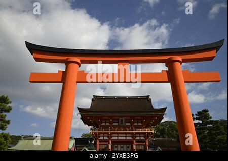 Vista panoramica di una gigantesca porta torii vermiglio di fronte alla porta rōmon presso il santuario shintoista Fushimi inari-taisha a Kyoto, Giappone. Foto Stock