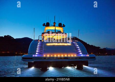 Yacht di lusso illuminato contro il cielo serale, navigando in acque tranquille circondate da paesaggi sereni. Foto Stock