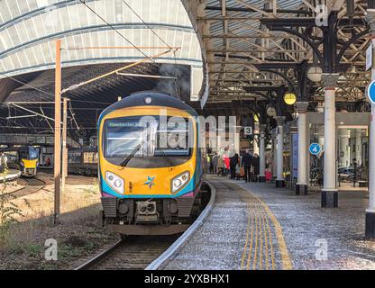 Un treno arriva a una fermata presso la piattaforma della stazione ferroviaria. Uno storico arco di ferro copre l'ingresso della stazione e i passeggeri aspettano di salire a bordo del treno Foto Stock