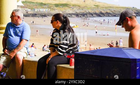 Barry Island, vale of Glam, Galles - luglio 26 2024: Due persone si siedono sul muro del rifugio occidentale sulla spiaggia di Barry Island durante una vacanza solare Foto Stock