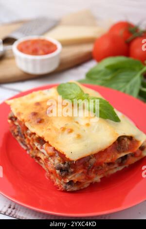 Un pezzo di deliziosa lasagna cotta con basilico sul tavolo, primo piano Foto Stock