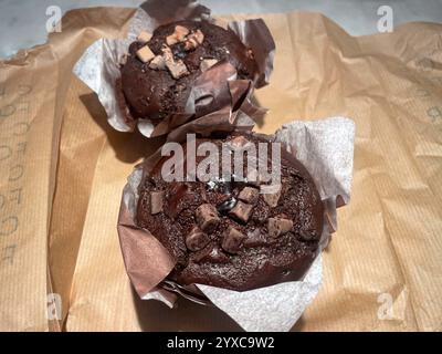 Due muffin al cioccolato vegan avvolti in carta pergamena, ricoperti da pezzi di cioccolato e un centro di cioccolato gooey, posto su carta marrone. Monaco ai Foto Stock