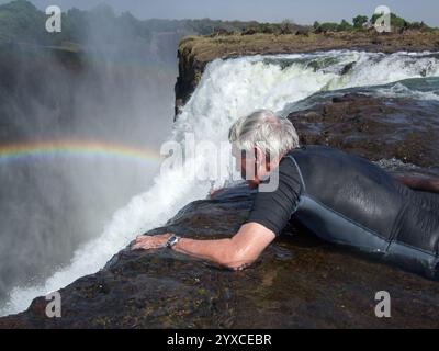 Uomo anziano sdraiato in acqua che guarda oltre il bordo delle Cascate Vittoria a devil's Pool, Livingstone Island, Zambesi River, Zambia, Africa Foto Stock