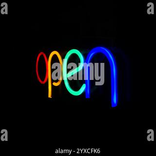 Un vivace cartello al neon con lettere rosse, gialle, verdi e blu luminose, fotografate con una leggera angolazione su sfondo nero. Foto Stock