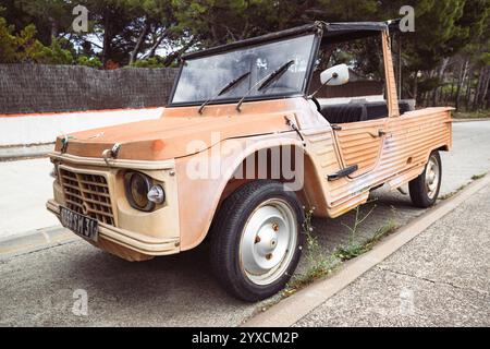 Un'antica auto Citroën Méhari Cabriolet color arancio parcheggiata su una strada di fronte a pini al sole sulla costa mediterranea Foto Stock