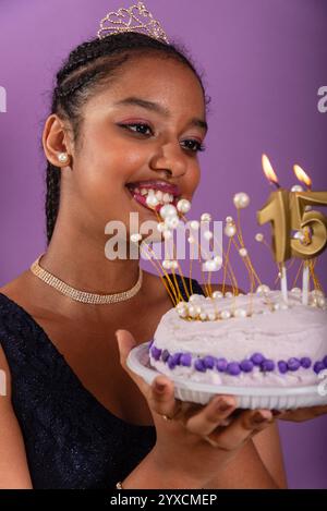 Una bruna adolescente che tiene una torta di compleanno e posa per una foto. Isolato su sfondo lilla. Foto Stock