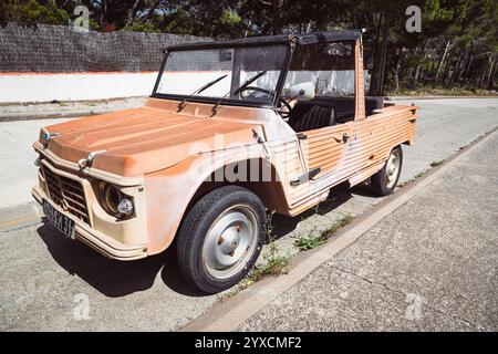 Un'antica auto Citroën Méhari Cabriolet color arancio parcheggiata su una strada di fronte a pini al sole sulla costa mediterranea Foto Stock