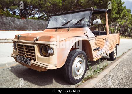 Un'antica auto Citroën Méhari Cabriolet color arancio parcheggiata su una strada di fronte a pini al sole sulla costa mediterranea Foto Stock