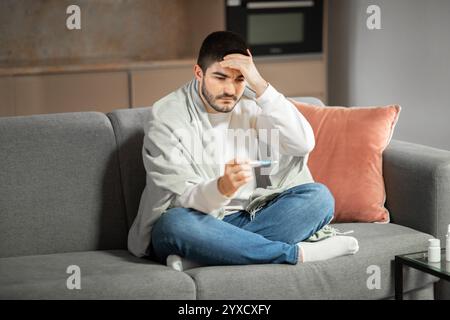 Il giovane si sente male a casa mentre controlla la temperatura Foto Stock