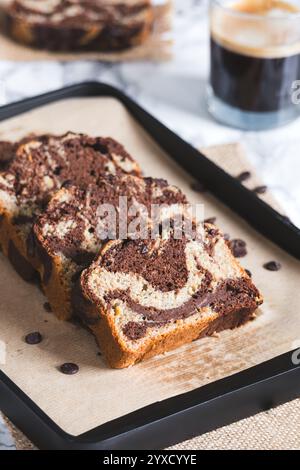 Primo piano di pane in marmo di cioccolato appena tagliato a fette di farina integrale e farro e un bicchiere di espresso sullo sfondo. Perfetto per chi ha problemi di salute Foto Stock