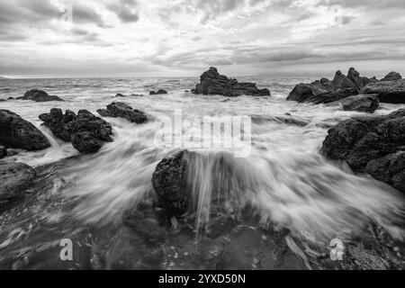 Un bellissimo tramonto sull'oceano con vista grandangolare delle rocce del Mare e Un'onda che si infrangono sulla costa in bianco e nero Foto Stock