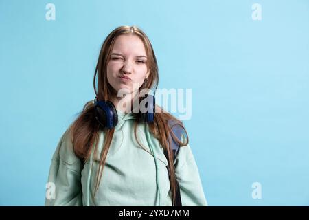 Giovane che fa strane espressioni facciali infantili, recita divertente e giocosa, isolata sullo sfondo dello studio. Adolescente infantile che fa facce stravaganti e si diverte Foto Stock