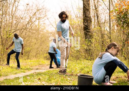 Giovane attivista che usa il rastrello per ripulire le foglie morte dai boschi, preservando l'ecosistema naturale e piantando alberi. Uomo che lavora volontariamente per un progetto di conservazione, rastrellando terreno. Foto Stock