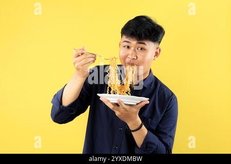 Giovane studente asiatico che tiene piatto bianco con tagliatelle fritte istantanee, mangiare con faccia felice Foto Stock