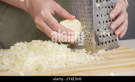 lo chef grattugia la tradizionale mozzarella con grattugia in acciaio sul pannello di legno. Foto Stock