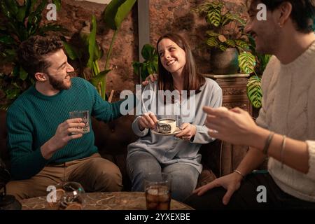 Gli amici si godranno un drink serale presso un caffè alla moda con pareti in mattoni a vista e piante tropicali. Riunione sociale informale che cattura l'amicizia autentica Foto Stock