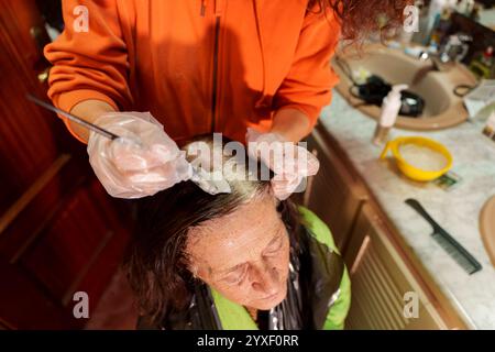 Donna anziana che riceve la copertura dei capelli grigi da un parrucchiere che indossa guanti e utilizza una spazzola colorante Foto Stock