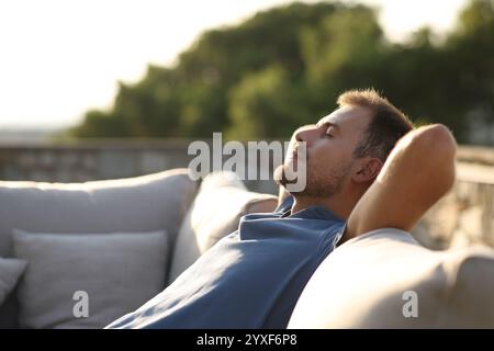 Vista laterale ritratto di un uomo rilassato seduto su un divano esterno in una casa o sulla terrazza dell'hotel Foto Stock