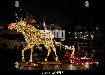 Nijmegen, Paesi Bassi. 15 dicembre 2024. La gente guarda una slitta illuminata trainata da una grande renna. Sculture di luce di diverse forme sono state collocate intorno al centro della città per celebrare il Natale. Quest'anno, un murale leggero ha onorato la vita degli artisti olandesi, Van Lymborch Brothers, nati a Nijmegen, a metà del XIV secolo. Credito: SOPA Images Limited/Alamy Live News Foto Stock