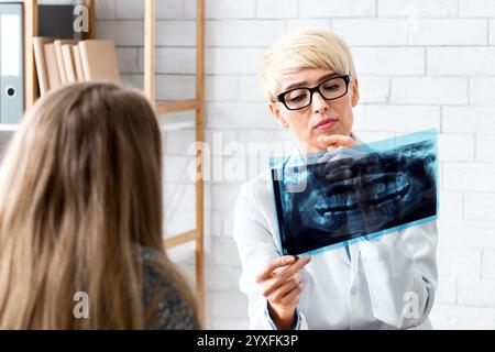 Donna dentista esamina radiografia del paziente all'interno dell'ufficio Foto Stock