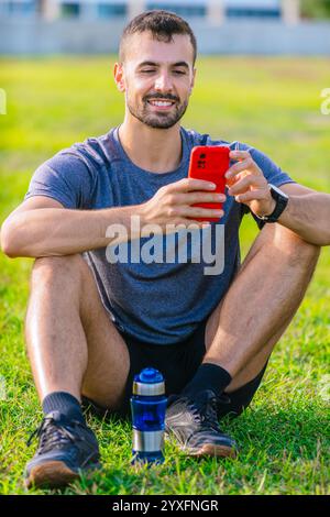 Uomo che utilizza lo smartphone mentre è seduto sull'erba nel parco all'aperto Foto Stock