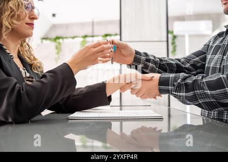 Donna d'affari che consegna le chiavi della casa al cliente mentre stringe la mano dopo aver concluso un contratto per un nuovo investimento immobiliare Foto Stock