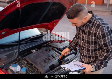 Agente assicurativo che ispeziona il motore di un'auto e completa la documentazione dopo un incidente stradale, valuta i danni e presenta un reclamo assicurativo Foto Stock