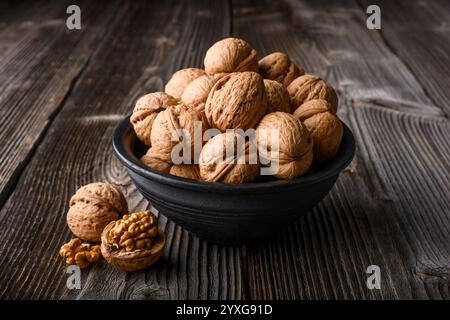 Noci di noce su una ciotola nera su un tavolo di legno da vicino. Fotografia gastronomica Foto Stock