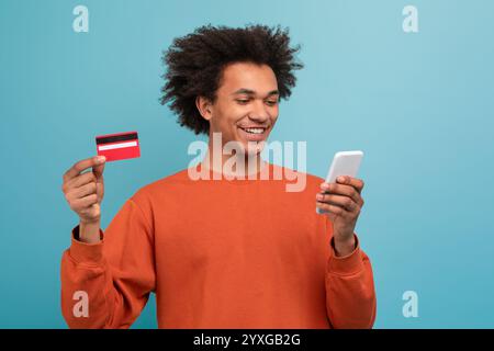 Il giovane con i capelli ricci usa lo smartphone mentre tiene in mano una carta di credito Foto Stock