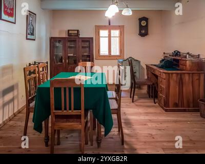 Sanok, Polonia - 4 maggio 2024. Un interno d'ufficio vintage con un tavolo in legno ricoperto da una tovaglia verde, circondato da sedie in legno. Foto Stock
