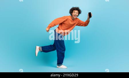 Gioioso uomo millenario balla con smartphone su sfondo blu Foto Stock