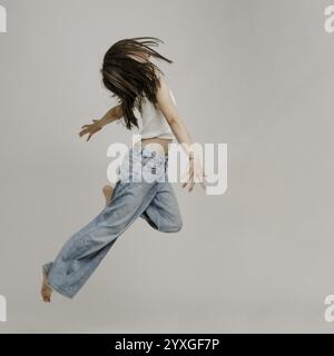 Ragazza dai capelli scuri, 10 anni, in jeans blu, salta Foto Stock