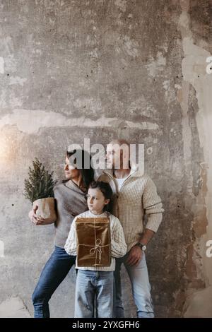 Famiglia con un piccolo albero di Natale e un regalo davanti a un muro di cemento Foto Stock