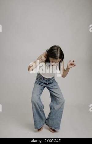 Ragazza dai capelli scuri, 10 anni, in Blue jeans, che fa una mossa divertente Foto Stock