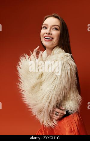 Una donna vivace posa con un sorriso brillante, indossando un elegante cappotto in pelliccia in un ambiente dai toni caldi. Foto Stock