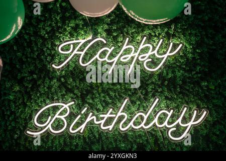 Cartello al neon per buon compleanno con muro d'erba e palloncini Foto Stock