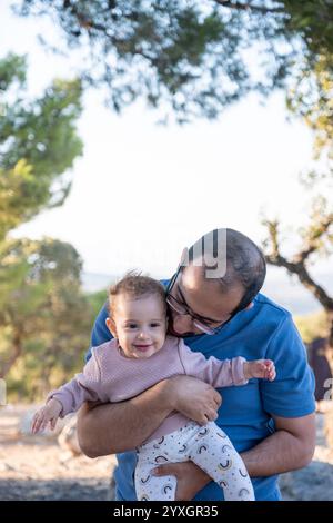 Un padre tiene il suo bambino sorridente in un ambiente tranquillo all'aperto. L'immagine cattura un momento gioioso di legame e felicità circondato dalla natura Foto Stock