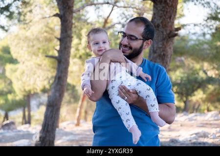 Un padre tiene il suo bambino sorridente in un ambiente tranquillo all'aperto. L'immagine cattura un momento gioioso di legame e felicità circondato dalla natura Foto Stock