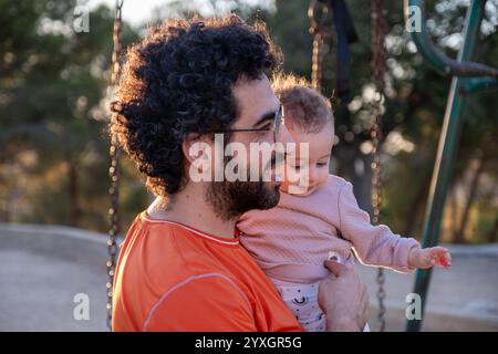 Un padre amorevole tiene il suo bambino mentre si diverte insieme in un parco soleggiato. Il momento cattura il calore, la connessione e la gioia della famiglia bondi Foto Stock