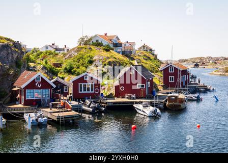 Paesaggio con tipici cottage dipinti di rosso e motoscafi ormeggiati in un molo di legno nella provincia di Bohuslän sulla costa occidentale svedese in una giornata di sole. Foto Stock