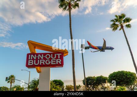 Insegna hamburger in-n-out vicino all'aeroporto LAX, con palme tipiche californiane e un aereo della Southwest Airlines che passa sopra Foto Stock