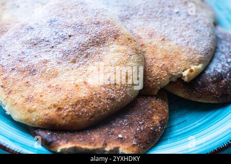 Le frittelle di formaggio con mirtilli rossi sono impilate su un piatto blu su un tavolo azzurro, cosparse di zucchero a velo. Foto di alta qualità Foto Stock