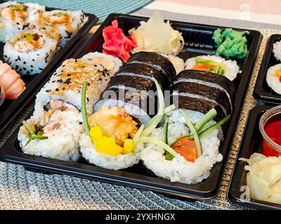 Ampio piatto di sushi con diversi panini, nigiri, maki, sashimi, salsa di soia, wasabi e zenzero sottaceto in vassoi di plastica, concetto di consegna di alimenti, o. Foto Stock