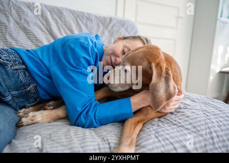 Amore incondizionato per il cane. Una donna rilassata abbraccia dolcemente il cane sul divano. Adozione animale per donna solitaria Foto Stock